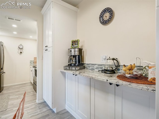 kitchen with white cabinets, light wood-type flooring, light stone countertops, and appliances with stainless steel finishes