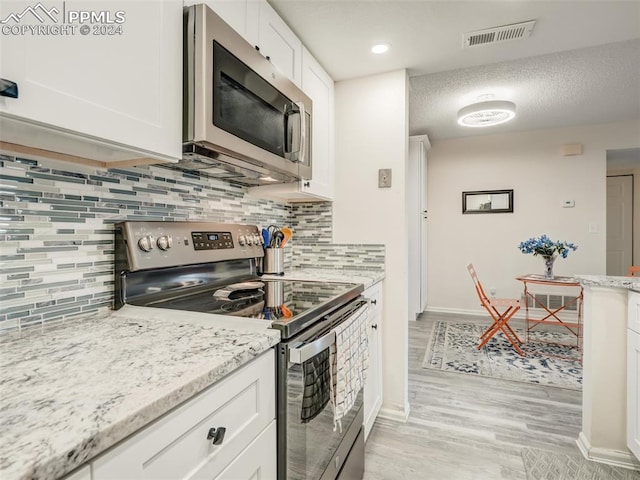 kitchen with light stone counters, backsplash, appliances with stainless steel finishes, white cabinets, and light wood-type flooring