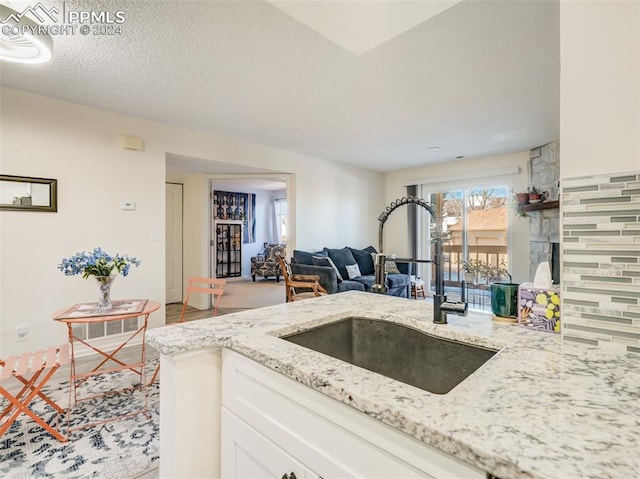 kitchen with light stone counters, white cabinetry, and sink