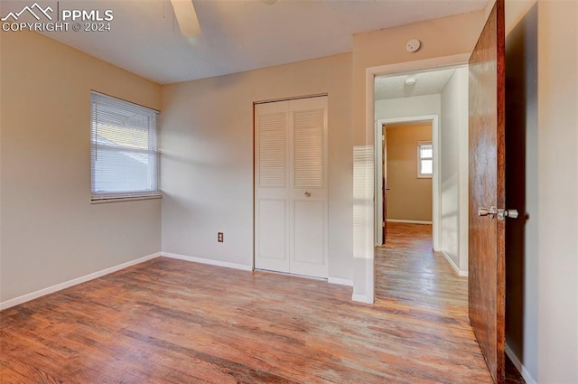 unfurnished bedroom featuring multiple windows, light hardwood / wood-style floors, ceiling fan, and a closet