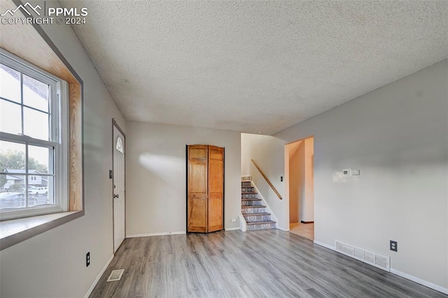 empty room with light wood-type flooring and a textured ceiling