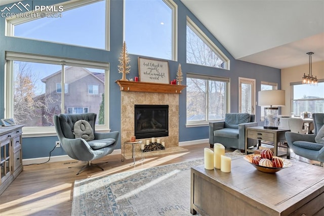 living room featuring a tile fireplace, light hardwood / wood-style floors, an inviting chandelier, and lofted ceiling