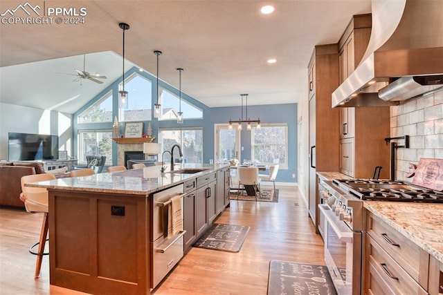 kitchen featuring sink, hanging light fixtures, wall chimney range hood, stainless steel stove, and light wood-type flooring