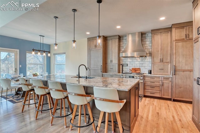 kitchen with premium appliances, wall chimney range hood, decorative light fixtures, light hardwood / wood-style floors, and a large island