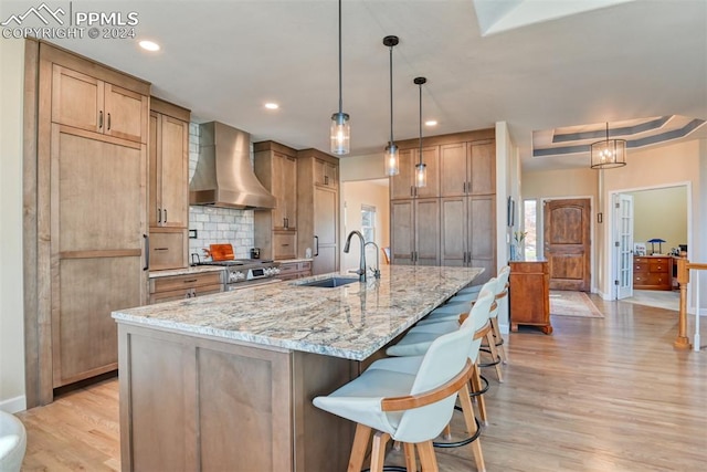 kitchen with a large island, light hardwood / wood-style floors, wall chimney range hood, and sink