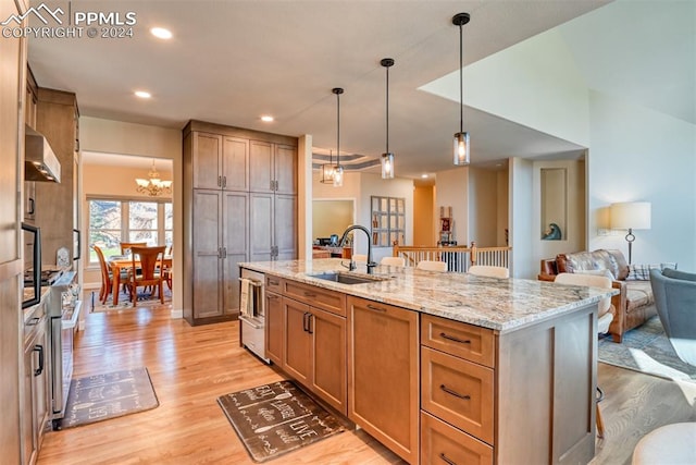 kitchen featuring a center island with sink, a kitchen breakfast bar, sink, hanging light fixtures, and light hardwood / wood-style flooring