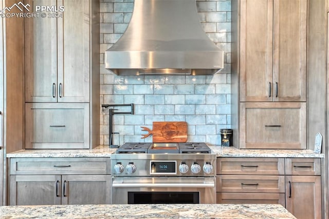 kitchen featuring wall chimney exhaust hood, light stone counters, high end stainless steel range, and tasteful backsplash