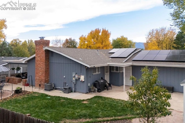 rear view of house with central AC unit, a patio area, solar panels, and a yard