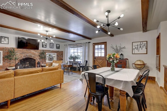 dining room featuring light wood-type flooring, beam ceiling, an inviting chandelier, and a brick fireplace