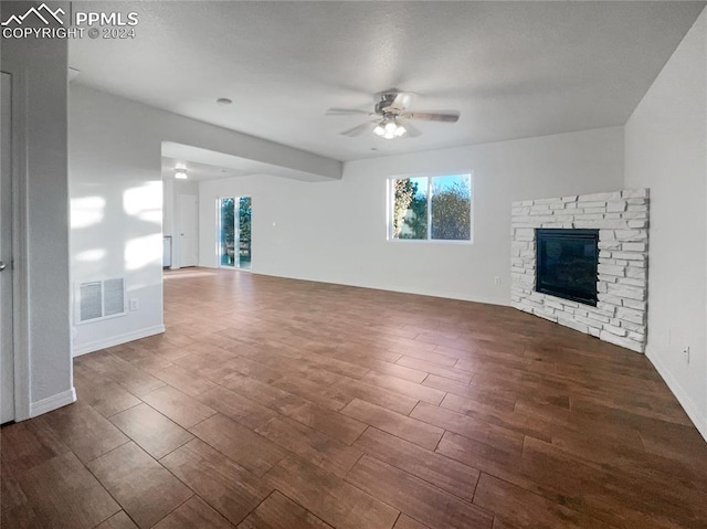 unfurnished living room with a stone fireplace, dark wood-type flooring, and ceiling fan