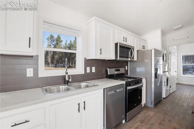 kitchen with stacked washer and clothes dryer, white cabinets, sink, decorative backsplash, and stainless steel appliances