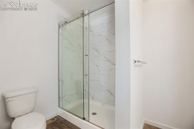 bathroom with hardwood / wood-style floors, toilet, and a shower with shower door