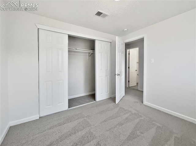 unfurnished bedroom featuring a textured ceiling, light carpet, and a closet