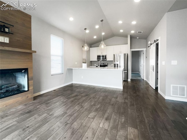 unfurnished living room with sink, lofted ceiling, a barn door, and dark hardwood / wood-style floors