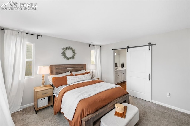 bedroom with a barn door, ensuite bathroom, multiple windows, and light carpet