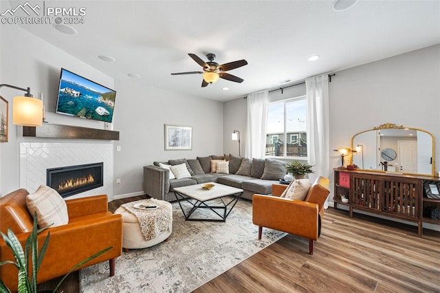 living room featuring hardwood / wood-style floors, a tiled fireplace, and ceiling fan