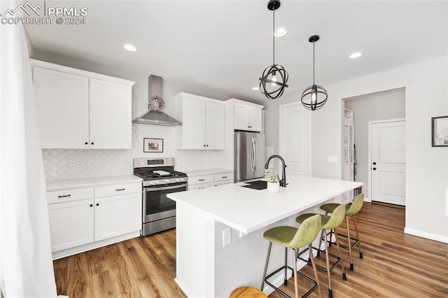 kitchen featuring a center island with sink, stainless steel appliances, light wood-type flooring, white cabinetry, and wall chimney range hood