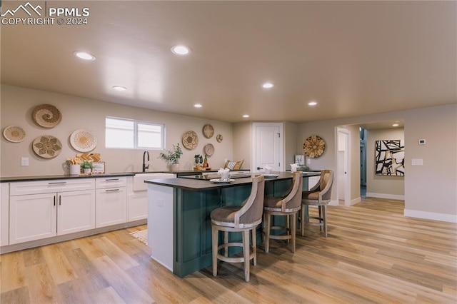 kitchen with a center island, sink, light hardwood / wood-style flooring, a breakfast bar area, and white cabinets