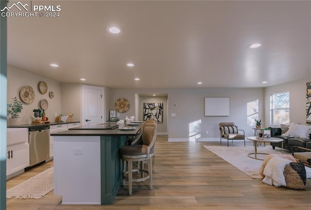 kitchen featuring dishwasher, white cabinets, black stovetop, light wood-type flooring, and a breakfast bar area