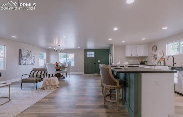 kitchen with dishwasher, an inviting chandelier, light hardwood / wood-style flooring, a kitchen bar, and white cabinets