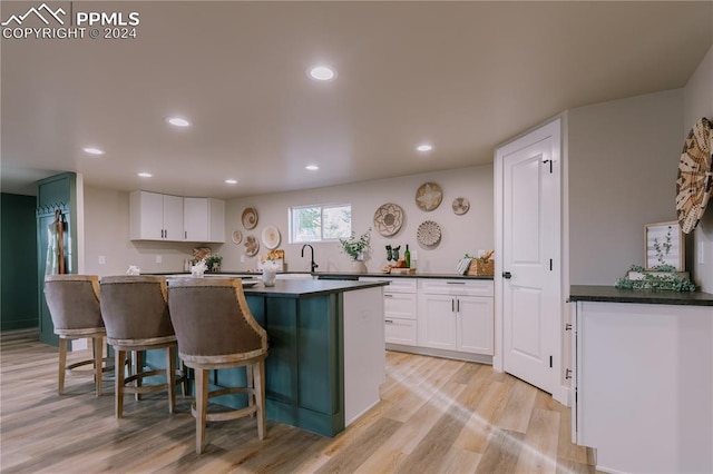 kitchen featuring a center island, white cabinets, a kitchen breakfast bar, sink, and light hardwood / wood-style floors