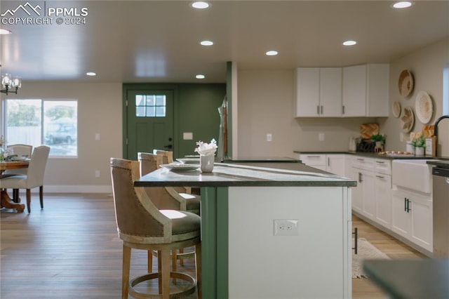 kitchen with sink, light wood-type flooring, a notable chandelier, a kitchen island, and white cabinetry