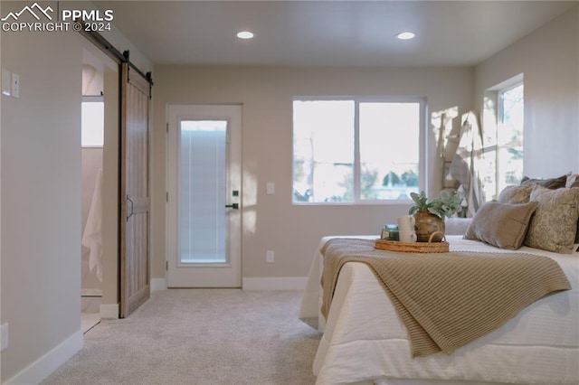 bedroom with a barn door, light carpet, and multiple windows