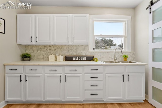 kitchen featuring sink, a barn door, tasteful backsplash, light hardwood / wood-style floors, and white cabinetry