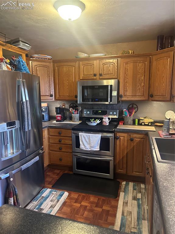 kitchen with dark parquet floors, sink, and appliances with stainless steel finishes