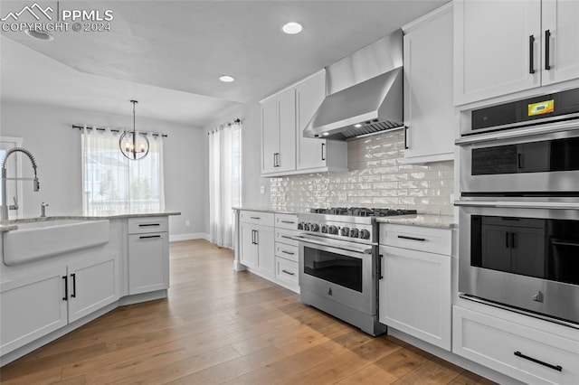 kitchen with wall chimney range hood, sink, light stone counters, white cabinetry, and stainless steel appliances