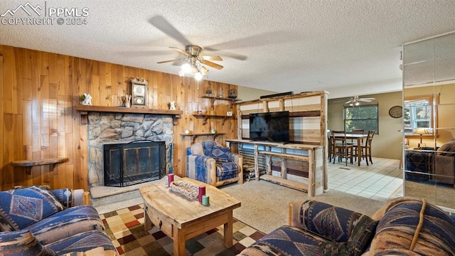 carpeted living room with a stone fireplace, wood walls, a textured ceiling, and ceiling fan