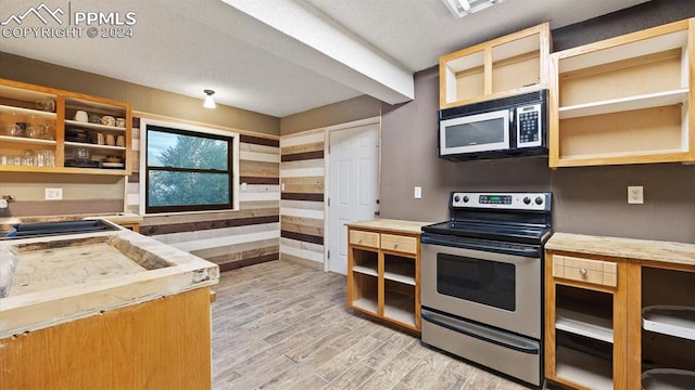 kitchen featuring wood walls, light hardwood / wood-style floors, sink, a textured ceiling, and stainless steel range with electric stovetop