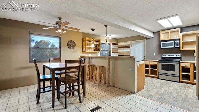 kitchen featuring a textured ceiling, hanging light fixtures, a breakfast bar, electric range, and ceiling fan