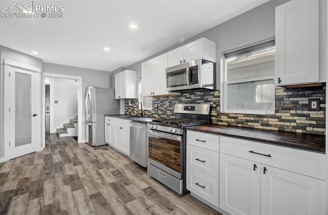 kitchen featuring decorative backsplash, stainless steel appliances, sink, white cabinets, and light hardwood / wood-style floors