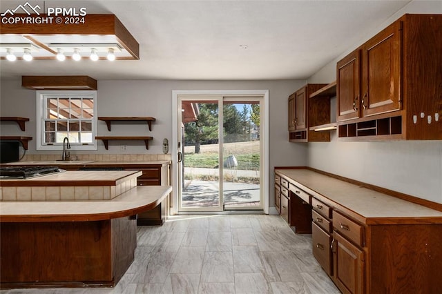 kitchen featuring stainless steel gas stovetop, built in desk, sink, tile counters, and a breakfast bar area