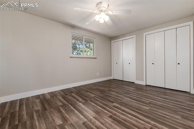 unfurnished bedroom featuring multiple closets, dark hardwood / wood-style floors, and ceiling fan