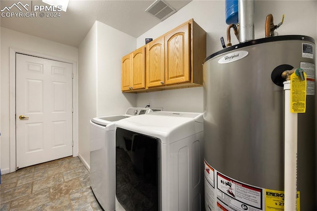 clothes washing area with cabinets, washer and clothes dryer, and water heater