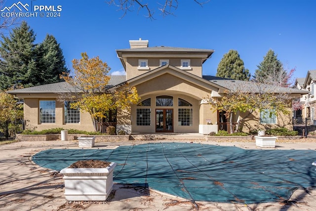 rear view of property featuring a covered pool, a patio, and french doors