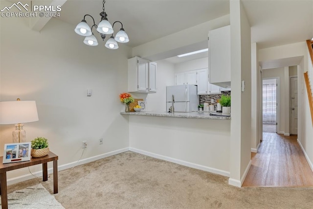 kitchen with an inviting chandelier, white refrigerator, decorative light fixtures, light colored carpet, and white cabinetry