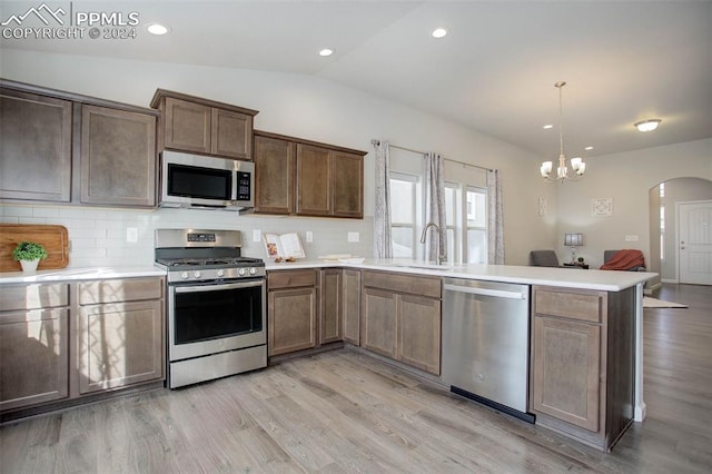 kitchen with stainless steel appliances, light wood-type flooring, pendant lighting, sink, and lofted ceiling