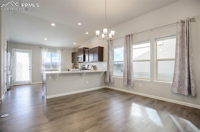 kitchen with appliances with stainless steel finishes, dark brown cabinetry, a breakfast bar, kitchen peninsula, and lofted ceiling