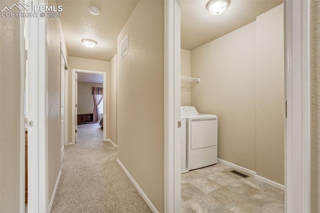 hallway featuring light colored carpet, a textured ceiling, and washing machine and clothes dryer