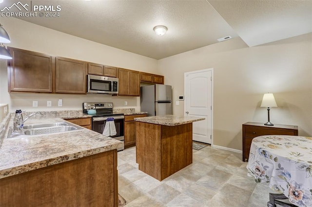 kitchen featuring stainless steel appliances, a kitchen island, a textured ceiling, decorative light fixtures, and sink