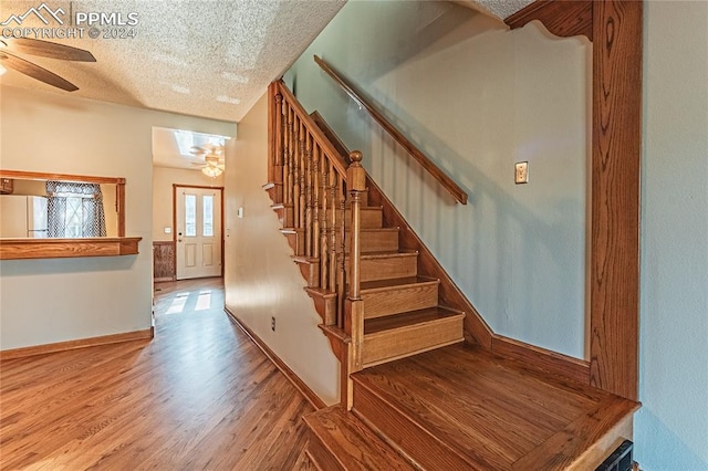 staircase featuring a textured ceiling, hardwood / wood-style flooring, and ceiling fan