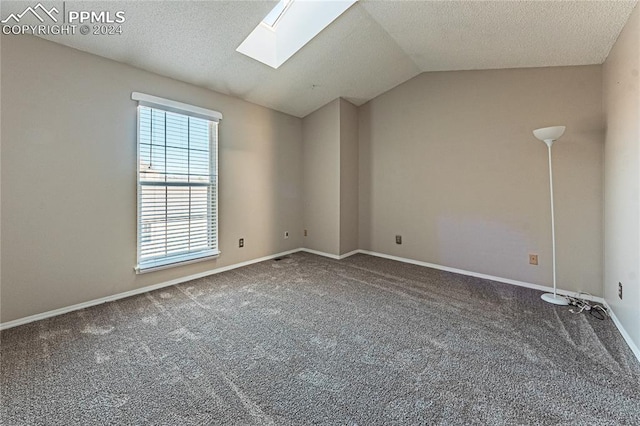 carpeted spare room with a textured ceiling and lofted ceiling with skylight