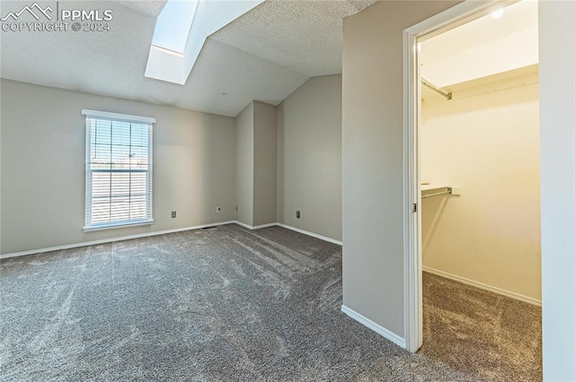 unfurnished bedroom with lofted ceiling with skylight, a spacious closet, a textured ceiling, and dark colored carpet