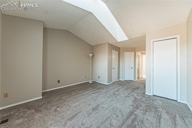 interior space featuring carpet, a textured ceiling, and vaulted ceiling with skylight