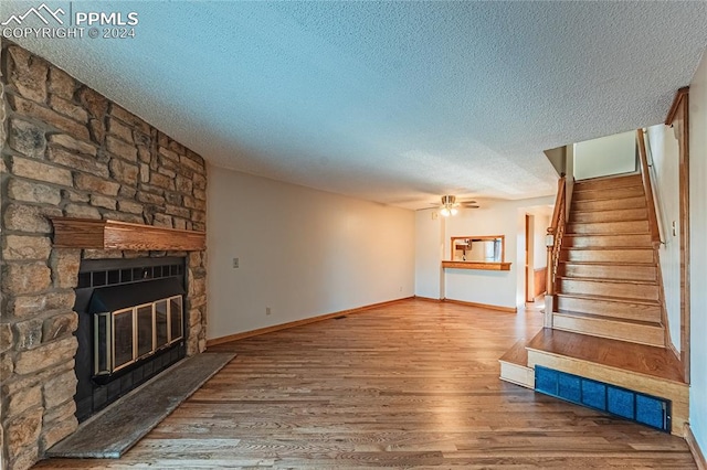 unfurnished living room featuring hardwood / wood-style floors, ceiling fan, a fireplace, and a textured ceiling