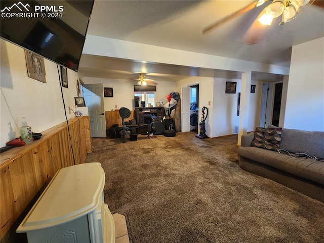 carpeted living room featuring ceiling fan, wood walls, and washer / dryer