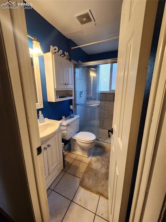 bathroom with tile patterned flooring, vanity, a shower with shower door, and toilet